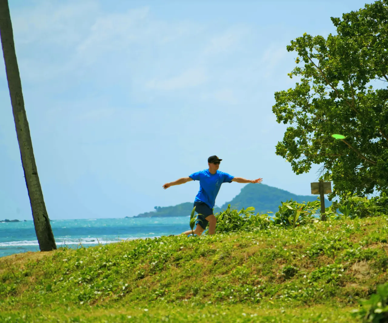 A player throws on the grassy bank above the sea, with an island behind, at Disc Golf Thailand, Koh Samui